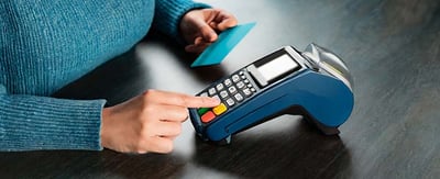 A woman's hand in blue sweater pushing buttons on a credit card POS machine