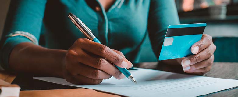 A woman's hands holding a credit card with one hand and writing a letter with the other