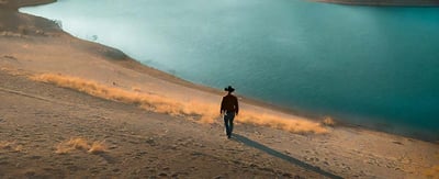 a cowboy walking near a lake