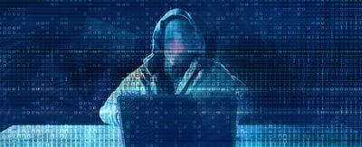 A faceless figure types on a laptop, the environment is dark and composed of blue, digital imagery